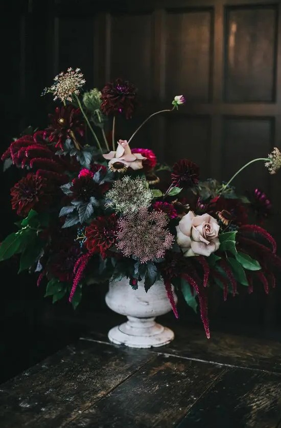 a vintage whitewashed vase with deep purple and burgundy blooms, pale roses, herbs and greenery