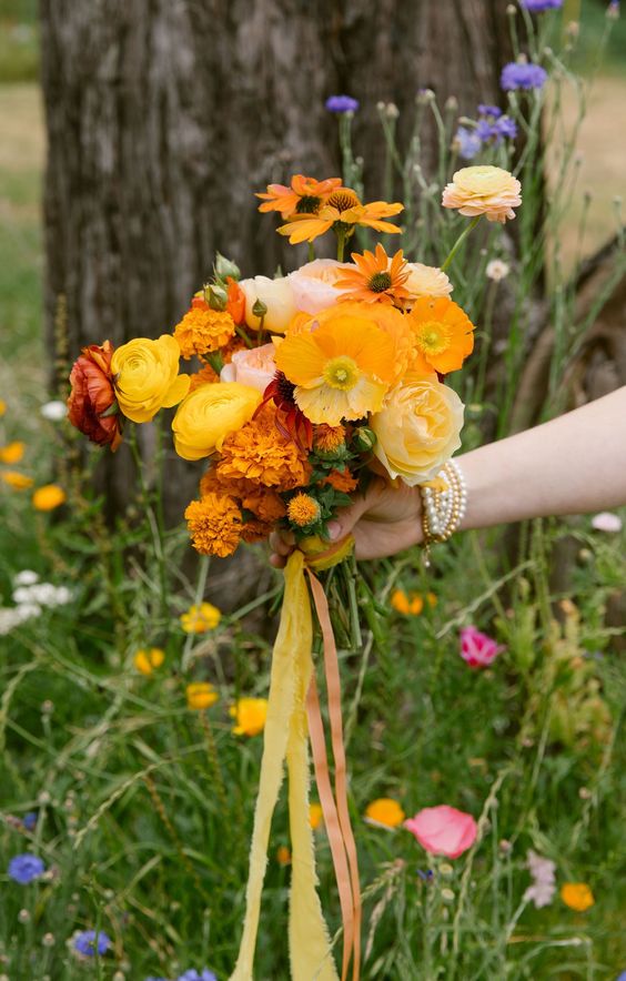 a bright summer wedding bouquet of ranunculus, poppies, marigolds and bright ribbons is a fun and bold idea
