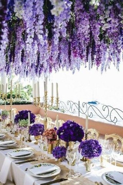 a refined and chic wedding tablescape with violet blooms and candelabras on the table and a gorgeous overhead floral installation of wisteria