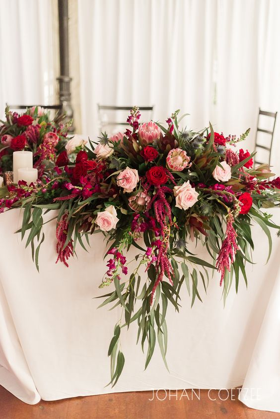 a bold wedding centerpiece of blush and red roses, king proteas, greenery and amaranthus is a lovely idea for the fall