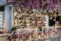 46 a refined and glam wedding reception space with a mirrored table and clear chairs, an oversized overhead wedding installation of white blooms and wisteria plus bulbs