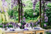 48 a romantic and relaxed outdoor wedding reception space with wisteria all over, with wooden furniture, wisteria and lilac on the table