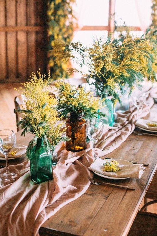 an effortlessly chic wedding tablescape with a blush table runner, colored bottles with mimosa, porcelain and glasses is lovely