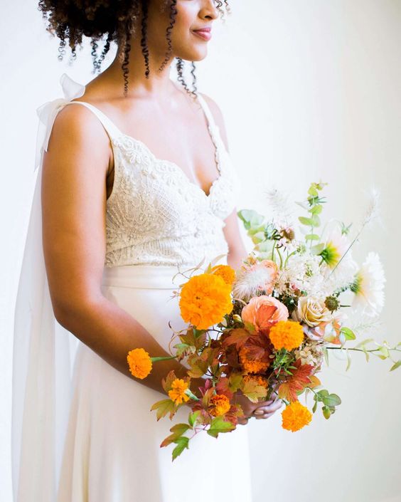 a catchy wedding bouquet of marigolds, white and neutral roses, greenery and a king protea is a sophisticated bride