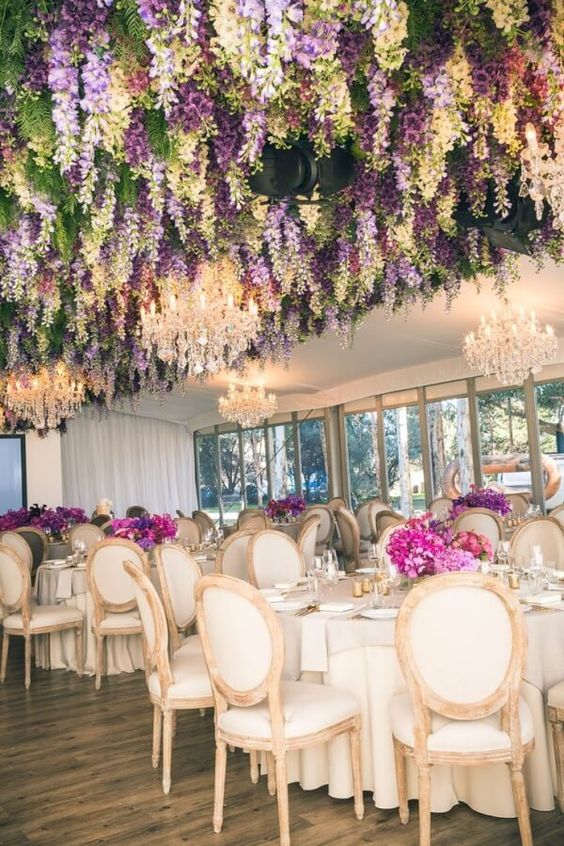 a sophisticated wedding reception space with greenery and wisteria hanging down, with fuchsia and purple blooms on the tables