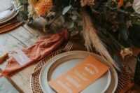 50 a bold retro inspired wedding tablescape with a woven placemat, neutral plates, orange napkins, a bold orange and neutral bloom centerpiece with greenery