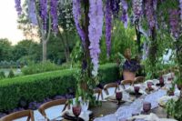 50 a super lush wedding reception space with an overhead floral installation with wisteria, a lilac table runner and purple glasses