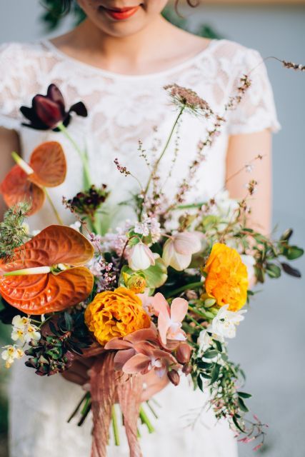 a colorful wedding bouquet of blush blooms, marigolds, tropical blooms, dark tulips and greenery and some relaxed and wild fillers