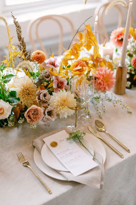 a bright fall wedding centerpiece of white and coral dahlias, orange mums, greenery, blush and white roses and bold fall leaves
