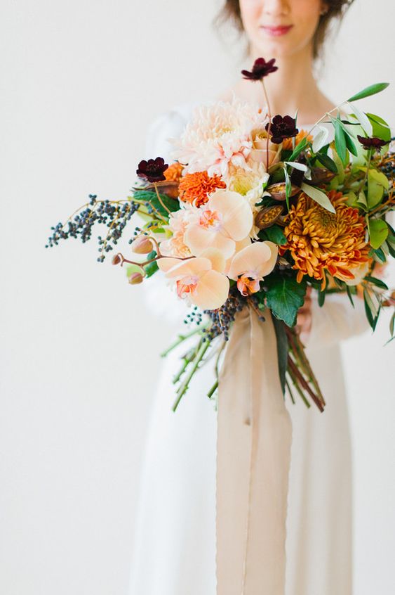 a contrasting wedding bouquet of blush orchids, large blush and orange dahlias, some marigolds, dark blooms, greenery and berries