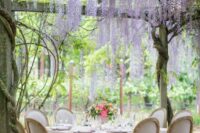 53 an intimate garden wedding reception space with a chic tablescape and matching chairs with bold blooms and wisteria hanging over the table