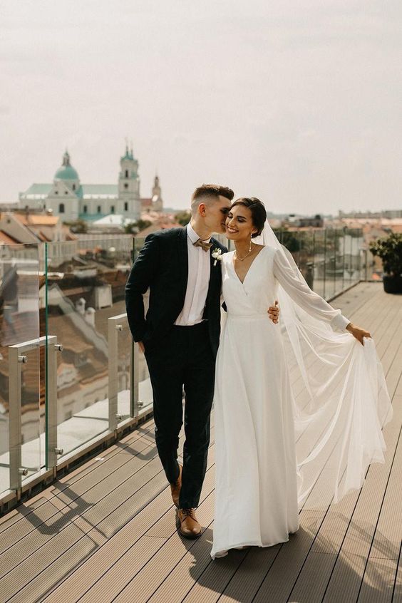 a modern A-line wedding dress with a V-neckline, long sleeves, a pleated skirt and a train are a cool combo for a modern wedding