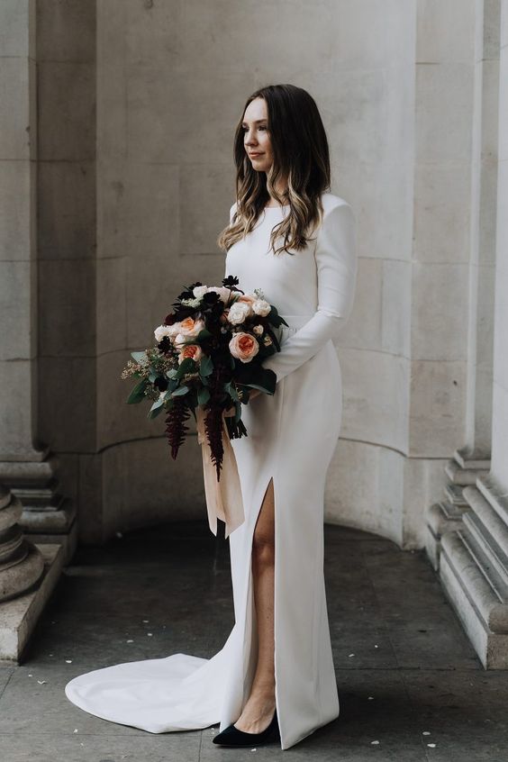 a modern and classic plain wedding dress with a high neckline, long sleeves, a slit and a train is a gorgeous idea for a modern wedding