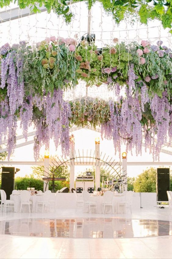 an oversized overhead chandelier over the dance floor, with greenery, wisteria, peachy and blush peony roses and lights