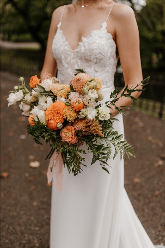 a dreamy fall wedding bouquet of marigolds, white roses and rust and orange dahlias, greenery and pink ribbons