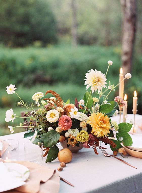 a colorful fall wedding centerpiece of white and yellow dahlias, coral blooms and leaves and fruit is amazing for a fall wedding