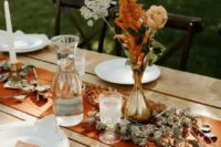 58 a cool and simple fall boho wedding centerpiece of a gilded vase, a blush rose, white and rust blooms, greenery on the table and a rust-colored table runner