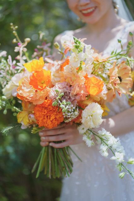 a lush summer wedding bouquet of orange poppies, marigolds, yellow tulips, white fillers and greenery feels wild