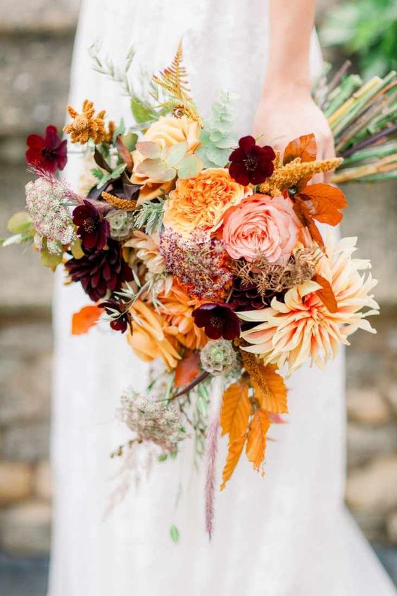 a bold contrasting wedding bouquet of marigolds, burgundy dahlias and pink and peachy roses, bold fall leaves, fillers and a bit of greenery