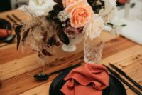 60 a dramatic fall wedding tablescape with rust napkins, black plates, a pretty bold floral centerpiece, black cutlery and neutral candles