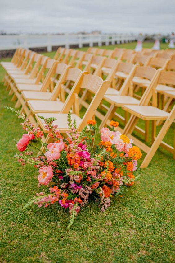 a colorful wedding aisle arrangement of coral peonies, marigolds and other blooms plus greenery is a cool idea for the summer