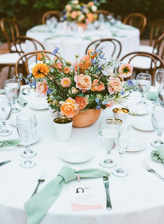a lovely wedding centerpiece of roses, marigolds, some blue fillers and greenery is a chic idea for a spring or summer wedding