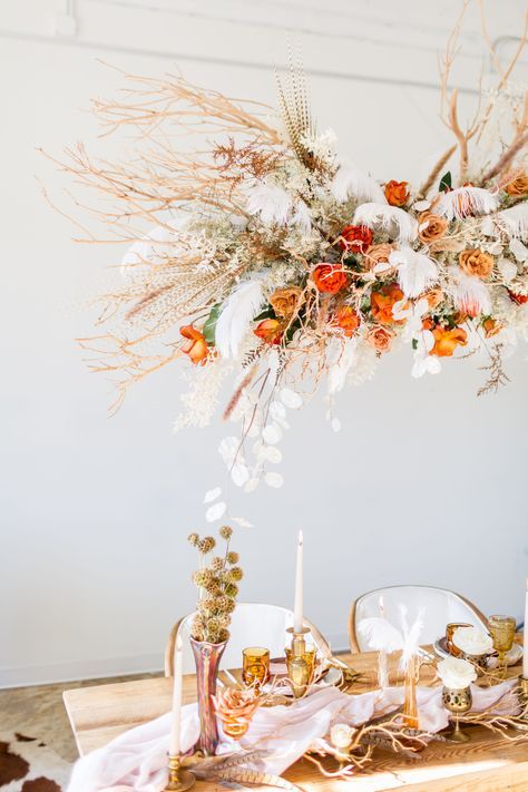 a lush wedding chandelier of lunaria, twigs and branches, feathers, greenery, marigolds and bold roses