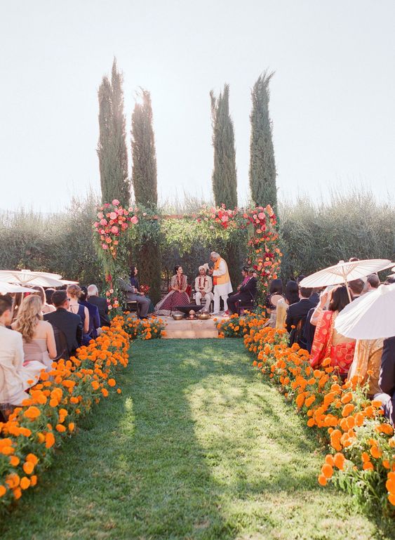 a super bold wedding space done with marigolds that line up the aisle and a bright pink wedding arch with greenery