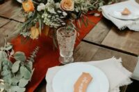 73 a beautiful boho fall wedding centerpiece of orange, burgundy, white blooms, greenery, a rust-colored table runner and candles around