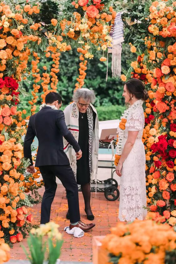 a super lush wedding arch with marigolds, pink and red roses and greenery and floral garlands cascading is a cool and bold idea