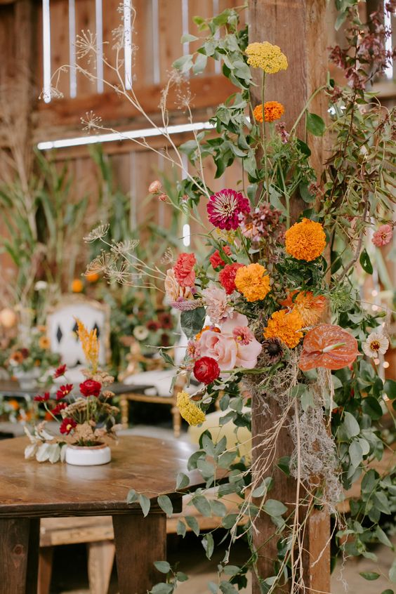 a wooden pillar decorated with greenery, marigolds, mums, roses and other blooms is a cool solution to make an indoor venue feel like outdoors