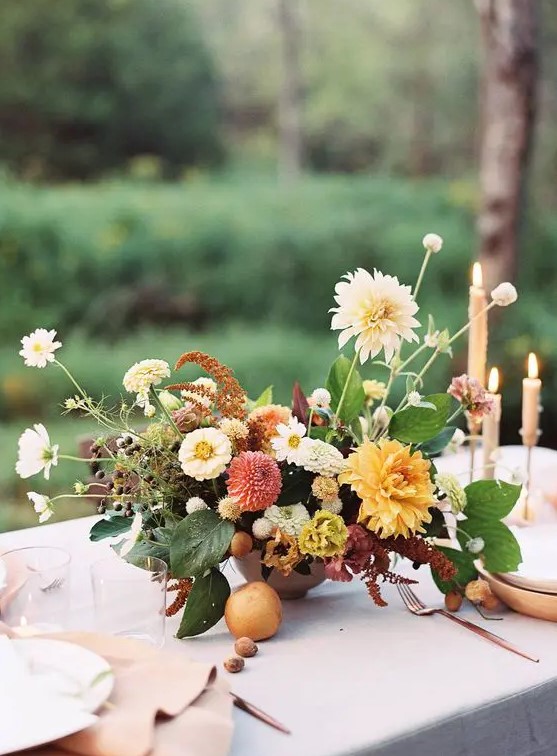 an elegant fall wedding centerpiece of red and orange dahlias, white blooms, berries, leaves and some fruit right on the table