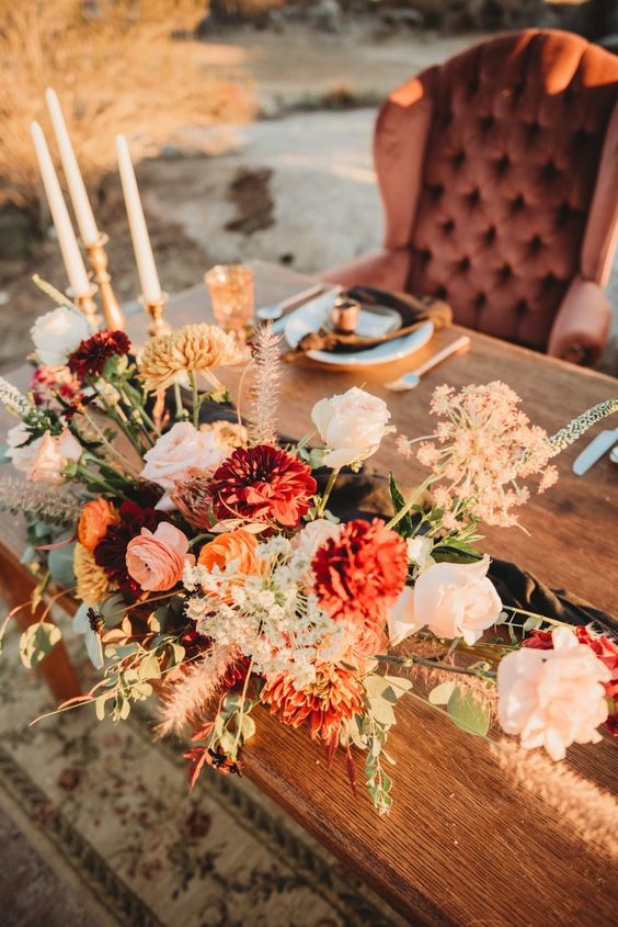 an exquisite boho fall wedding centerpiece of blush roses, burgundy mums and ranunculus, greenery and grasses is amazing for a fall celebration