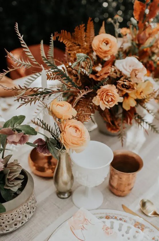 bold boho fall wedding centerpieces of orange, blush and rust blooms, greenery, bold foliage and candles around are cool