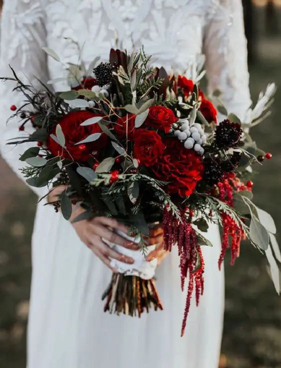 a Christmas wedding bouquet of red roses, deep purple blooms, berries and greenery plus a bit of amaranthus for an eye-catchy touch