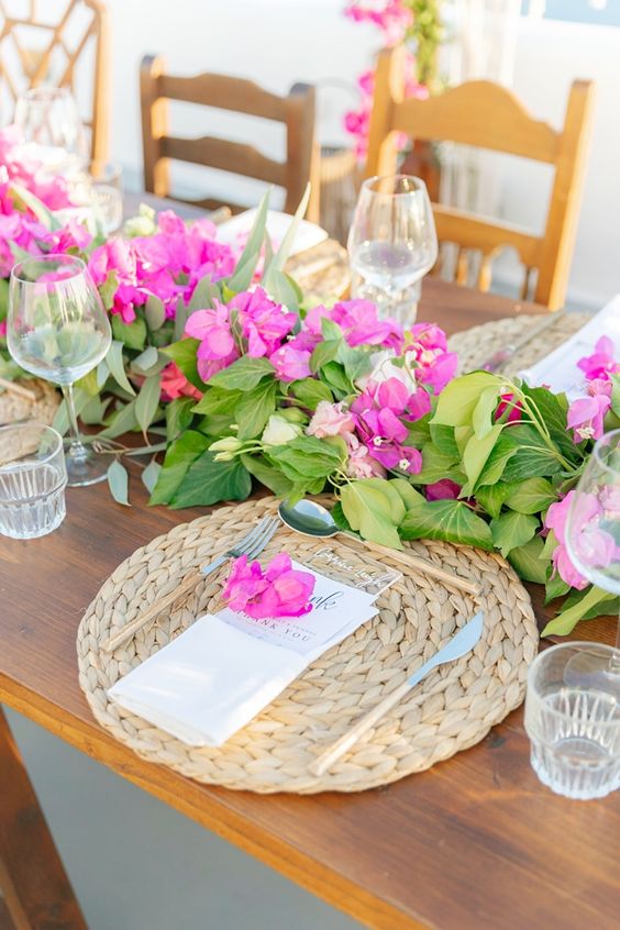 a Mediterranean wedding tablescape with a greenery, bougainvillea and rose runner, woven palcemats and simple glasses