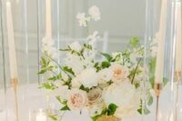 a beautiful and delicate wedding centerpiece of white and blush roses, greenery and white sweet peas plus candles around is amazing
