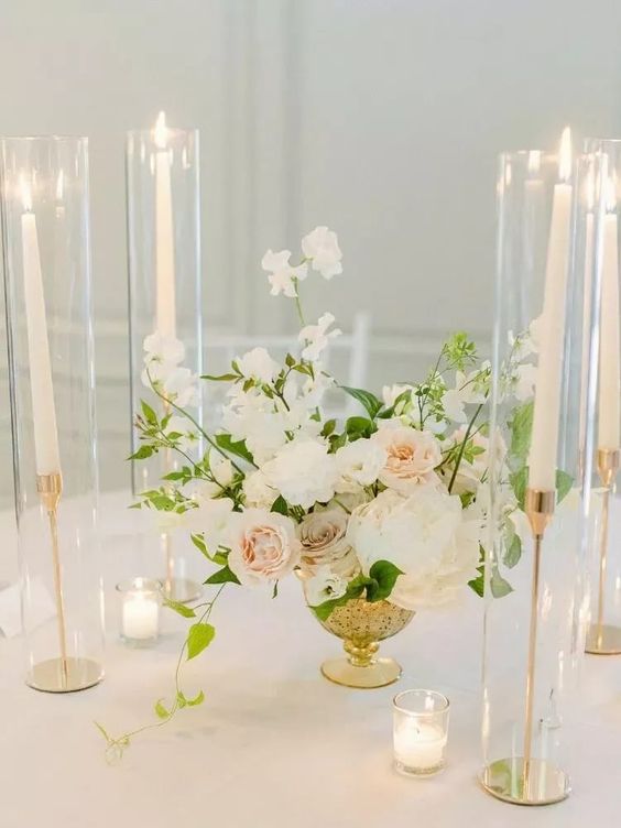 a beautiful and delicate wedding centerpiece of white and blush roses, greenery and white sweet peas plus candles around is amazing