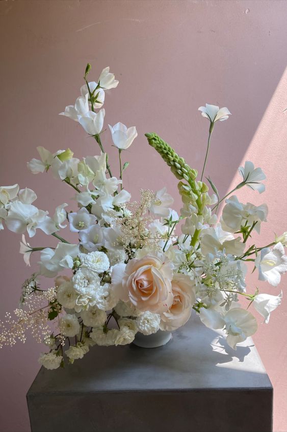 a beautiful neutral wedding centerpiece of blush roses, sweet peas and lots of other white blooms for spring or summer