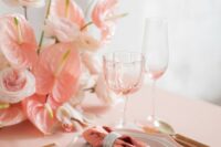 a beautiful pink wedding tablescape with a pink tablecloth and napkins, a pink wedding centerpiece of peony roses, anthurium and gold cutlery