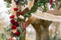 a boho rustic wedding arch done with macrame, greenery, pampas grass, blush and burgundy roses and dahlias and amaranthus
