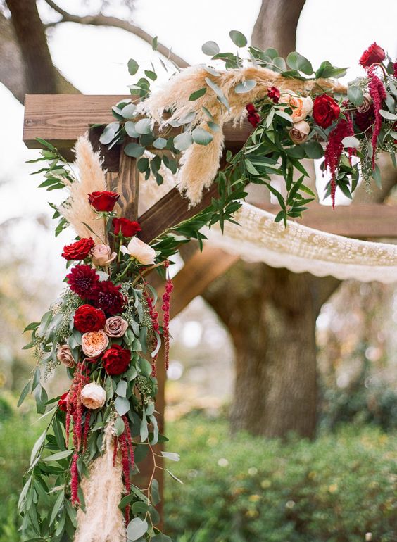 a boho rustic wedding arch done with macrame, greenery, pampas grass, blush and burgundy roses and dahlias and amaranthus