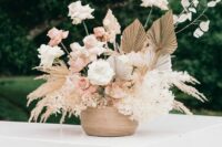a boho wedding centerpiece of pampas grass, white blooms, blush and white roses, lunaria, fronds is a very chic and cool arrangement