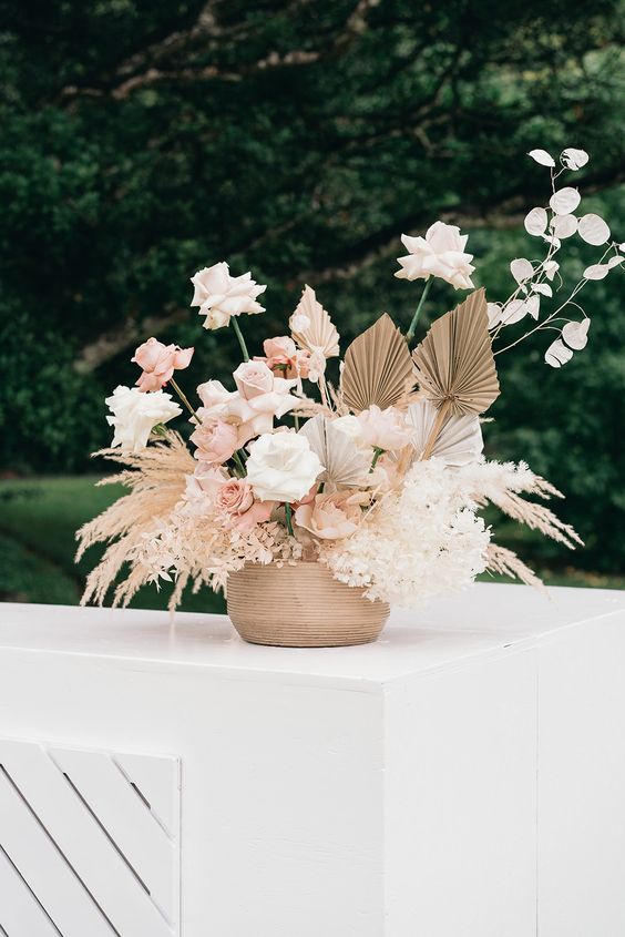 a boho wedding centerpiece of pampas grass, white blooms, blush and white roses, lunaria, fronds is a very chic and cool arrangement