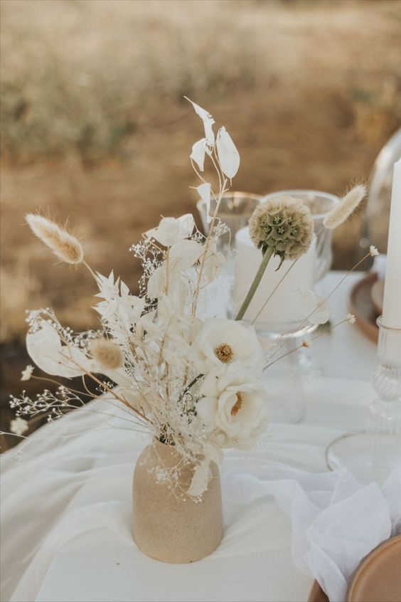 a boho wedding centerpiece of white blooms, seed pods, bunny tails, white leaves and blooms is a lovely idea