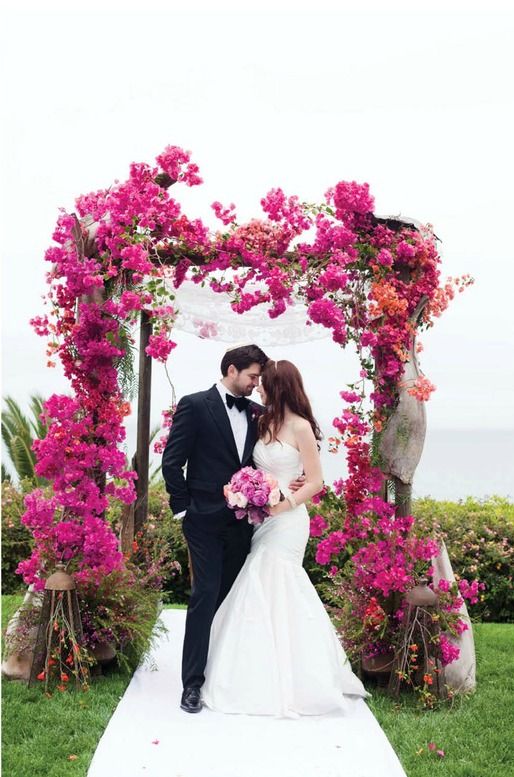 a bold and elegant wedding arch covered with bougainvillea is a lovely idea for a bright wedding and a sea view adds charm