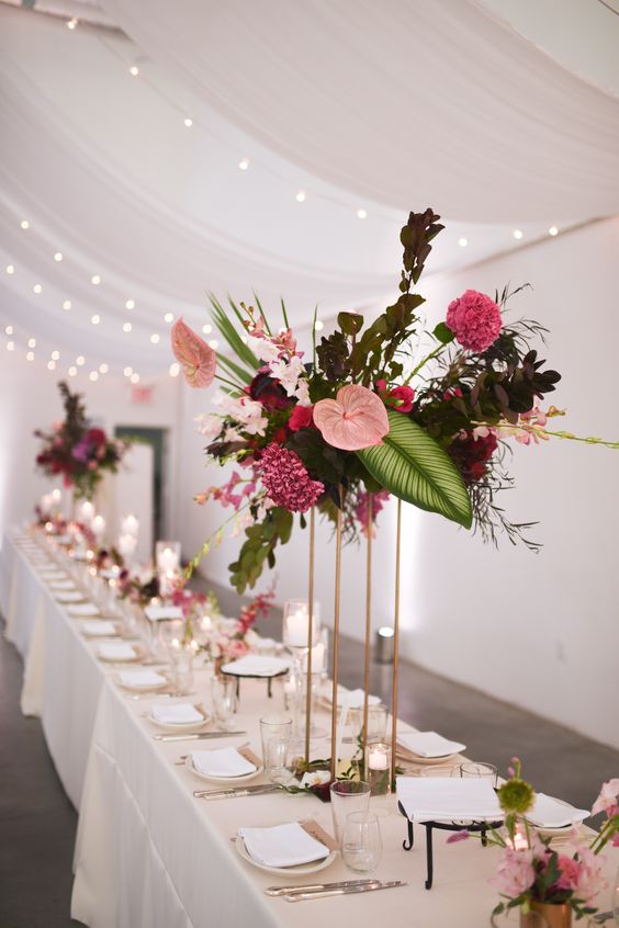 a bold and tall wedding centerpiece of leaves and foliage, pink carnations and pink anthuriums is amazing for a wedding