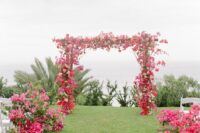 a bold boho wedding arch covered with bougainviilea and white roses and matching bougainviilea arrangements lining up the aisle