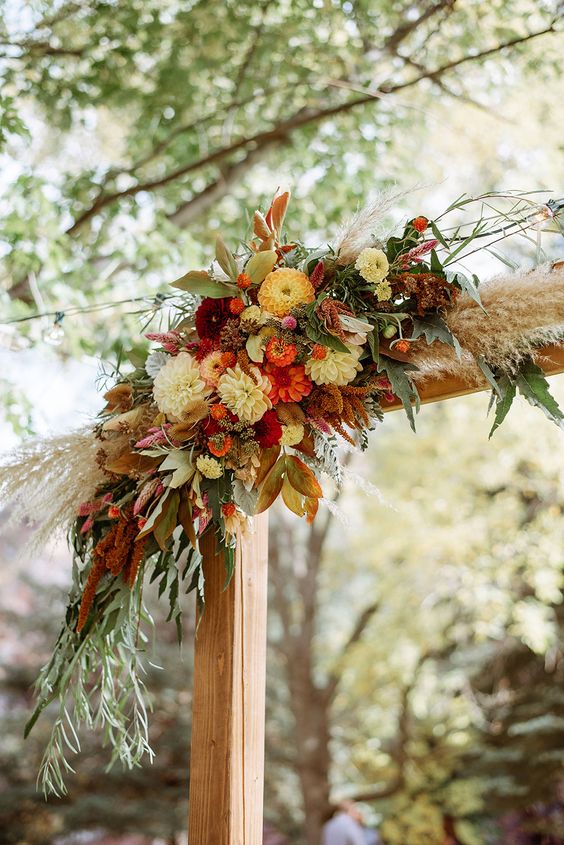 a bold rustic wedding arch with white and orange mums, berries, greenery, pampas grass, twigs and amaranthus for a fall wedding