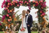 a bold tropical wedding arch covered with fronds, greenery, orange, blush, coral, pink peonies and roses and bougainvillea